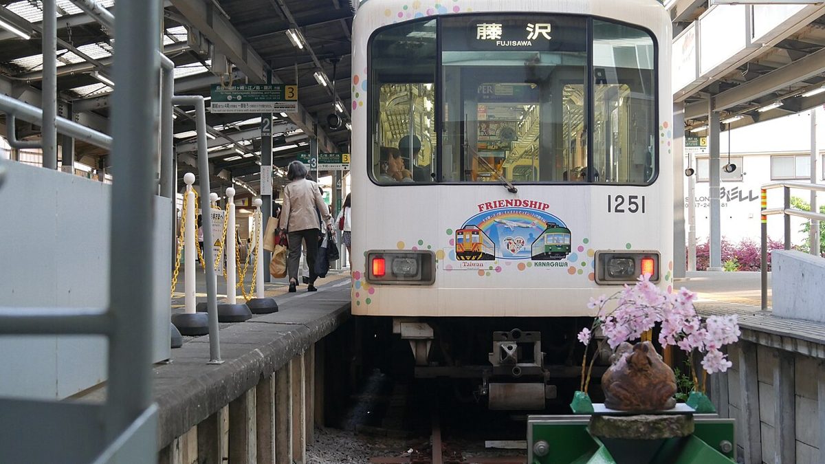 A green-and-cream Enoden train running along the Kamakura coast