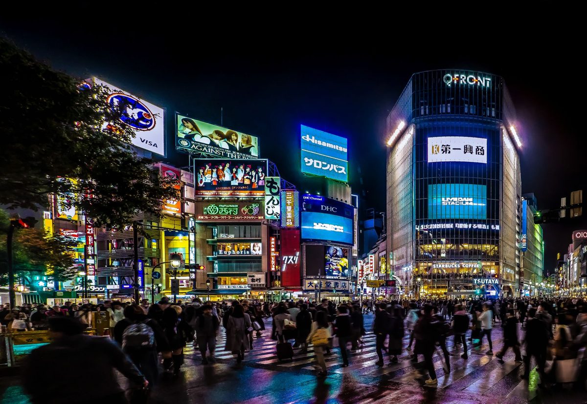 Crowds streaming across Shibuya Scramble Crossing under bright neon billboards at night