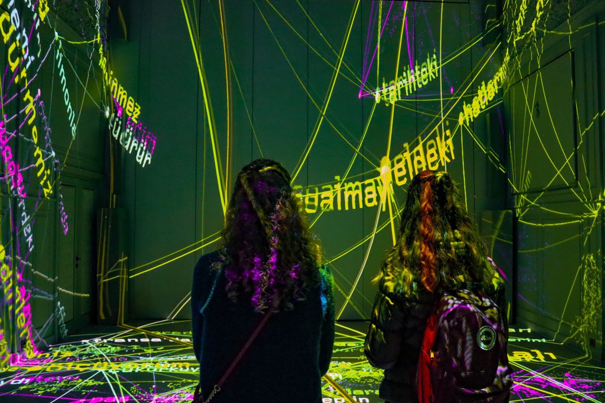 Projected flowers blooming across the floor and walls of a dark gallery