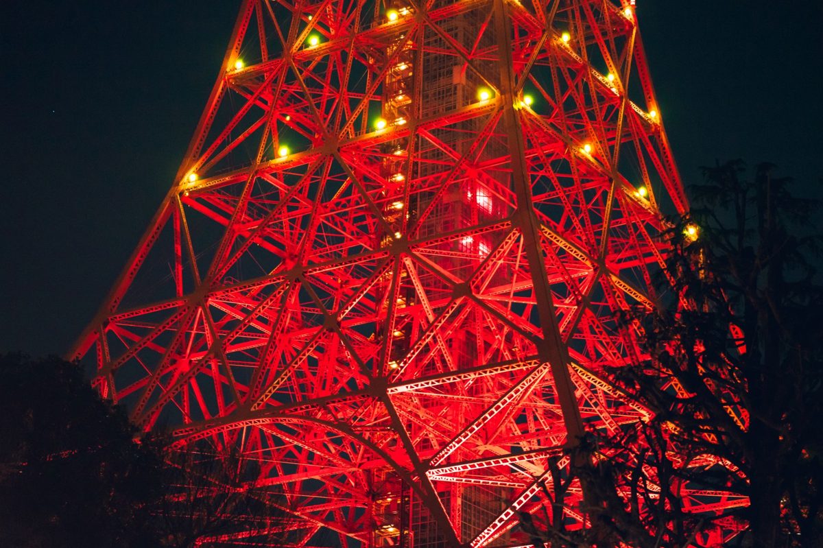 Tokyo Tower lit orange against the evening sky, seen between buildings