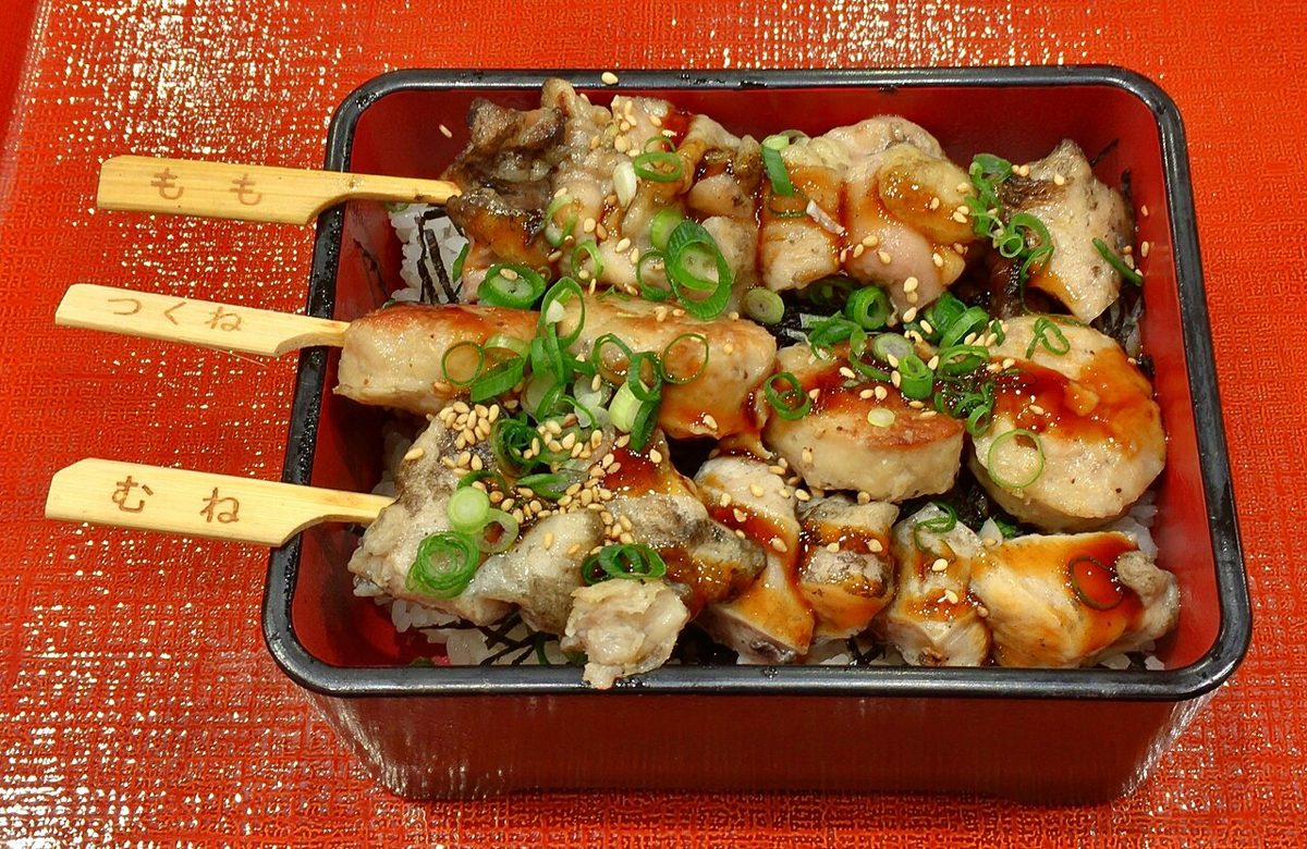 A yakitori chef grilling rows of chicken skewers over a charcoal grill