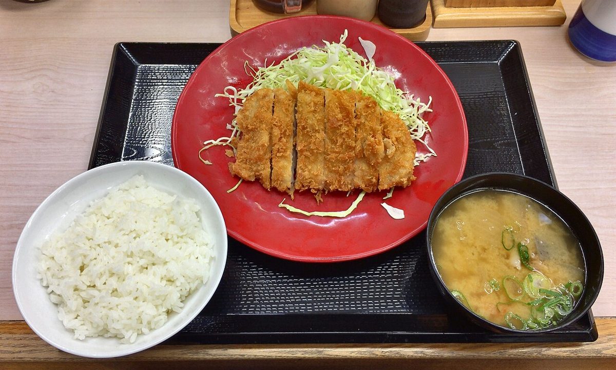 A complete tonkatsu teishoku set with rice, miso soup, cabbage and pickles on a tray