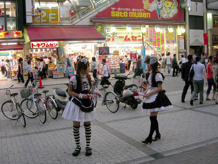 Two women in black and white maid costumes handing out flyers on a busy Akihabara street