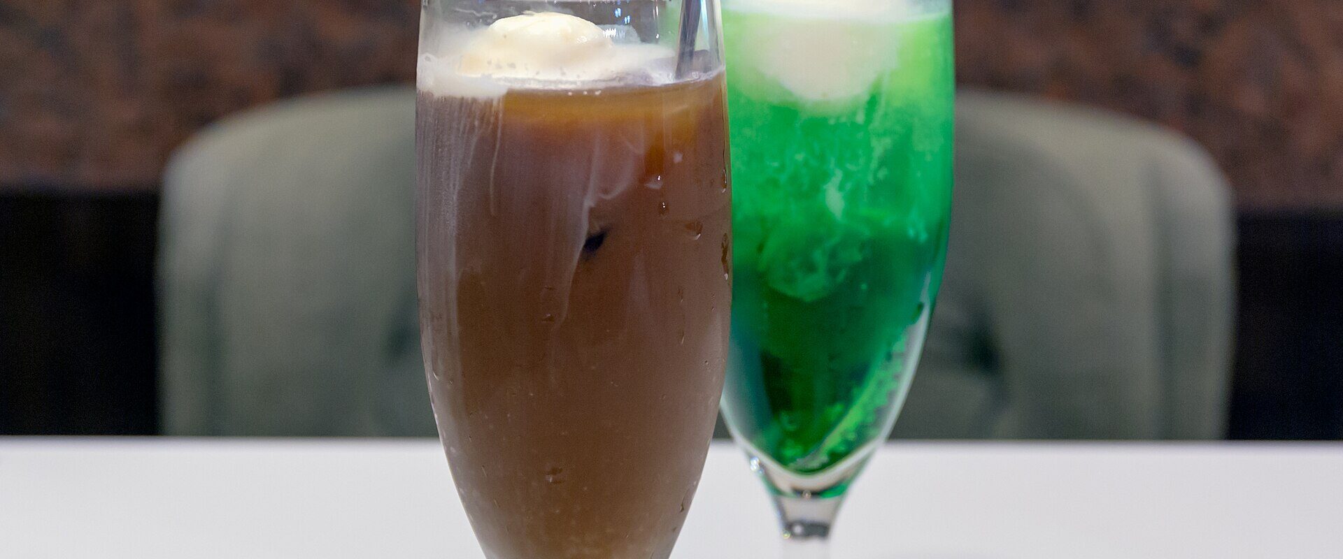 A coffee float and a green melon cream soda in tall glasses on a cafe table