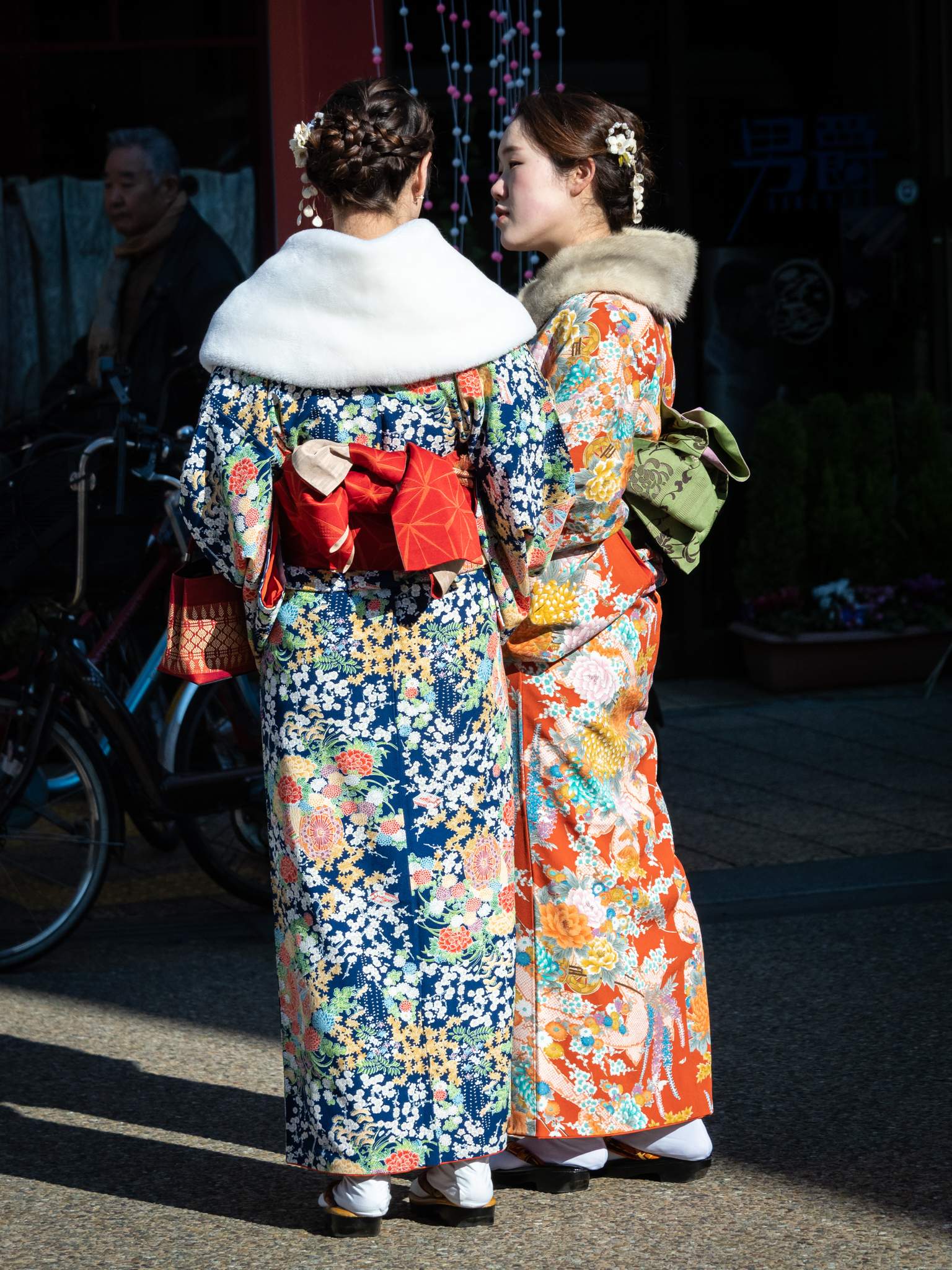 Two young women in brightly patterned furisode kimono with fur stoles on a street in Asakusa