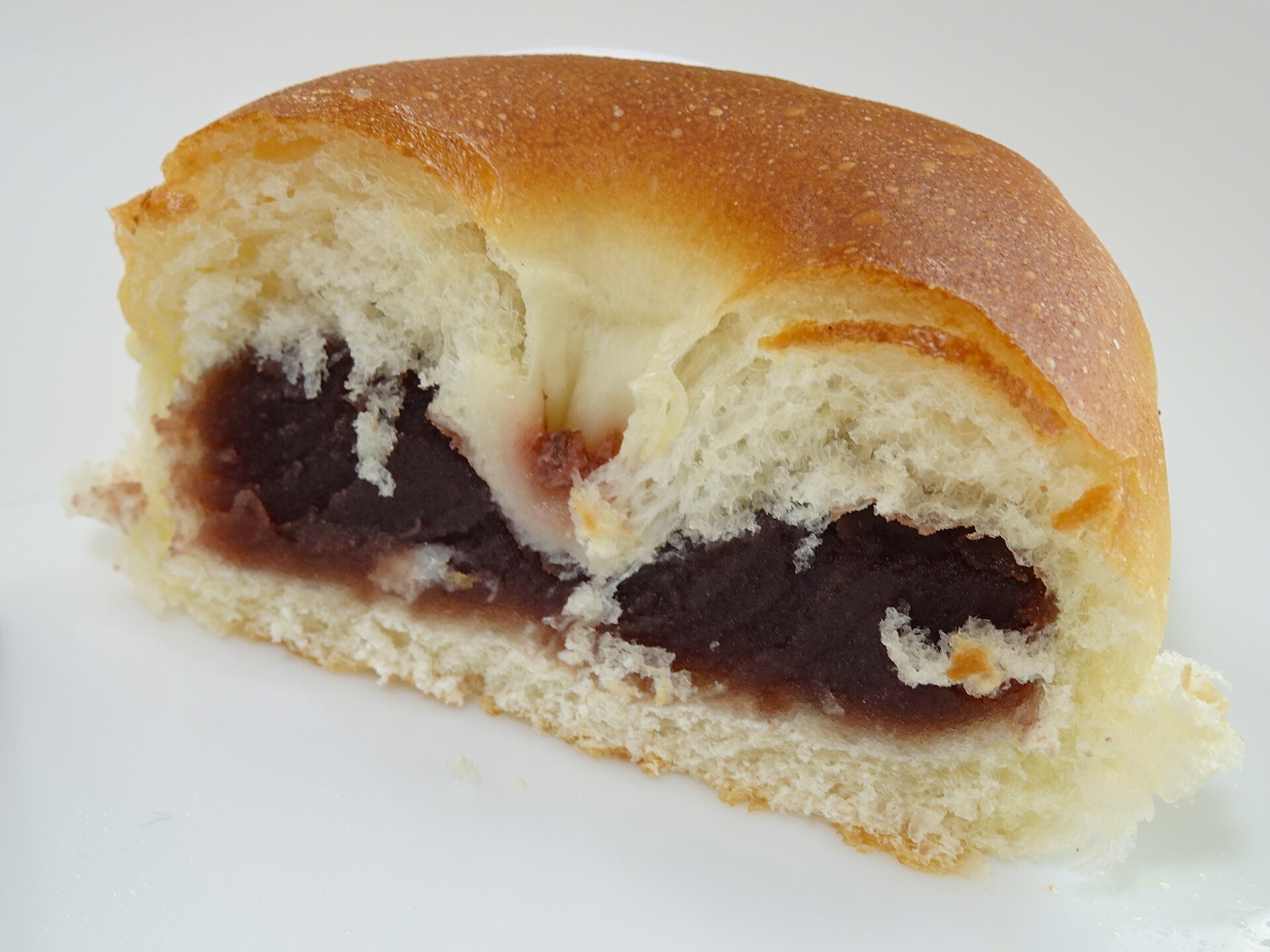 A sakura anpan from Ginza Kimuraya cut in half to show dark red bean paste inside a soft golden bun