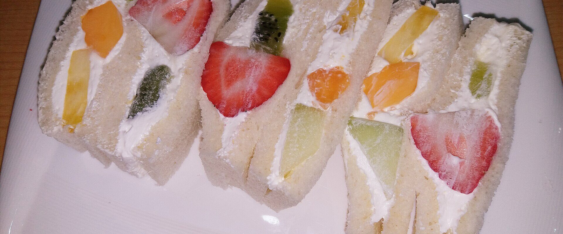 A plate of Japanese fruit sandwiches cut to show strawberries, kiwi, orange and melon set in whipped cream