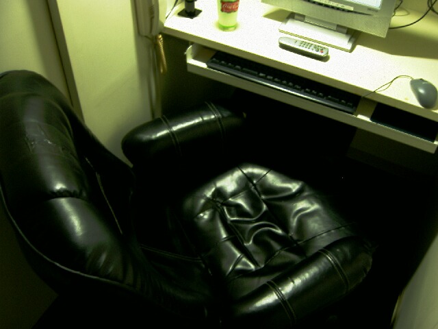 A small private booth in a Japanese internet cafe with a reclining leather chair, desk and computer