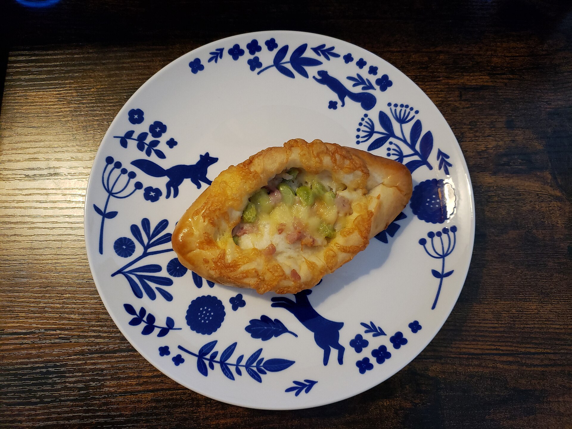 A boat-shaped savoury bread filled with bacon, edamame and melted cheese on a blue and white plate