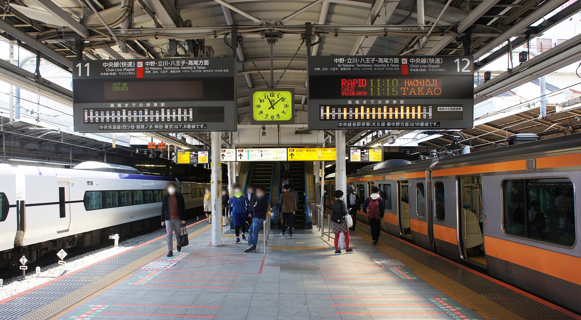 An orange-striped Chuo Line train and a white limited express train at platforms 11 and 12 inside JR Shinjuku Station