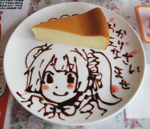 A slice of cheesecake on a plate decorated with a chocolate drawing of a girl and Japanese welcome text