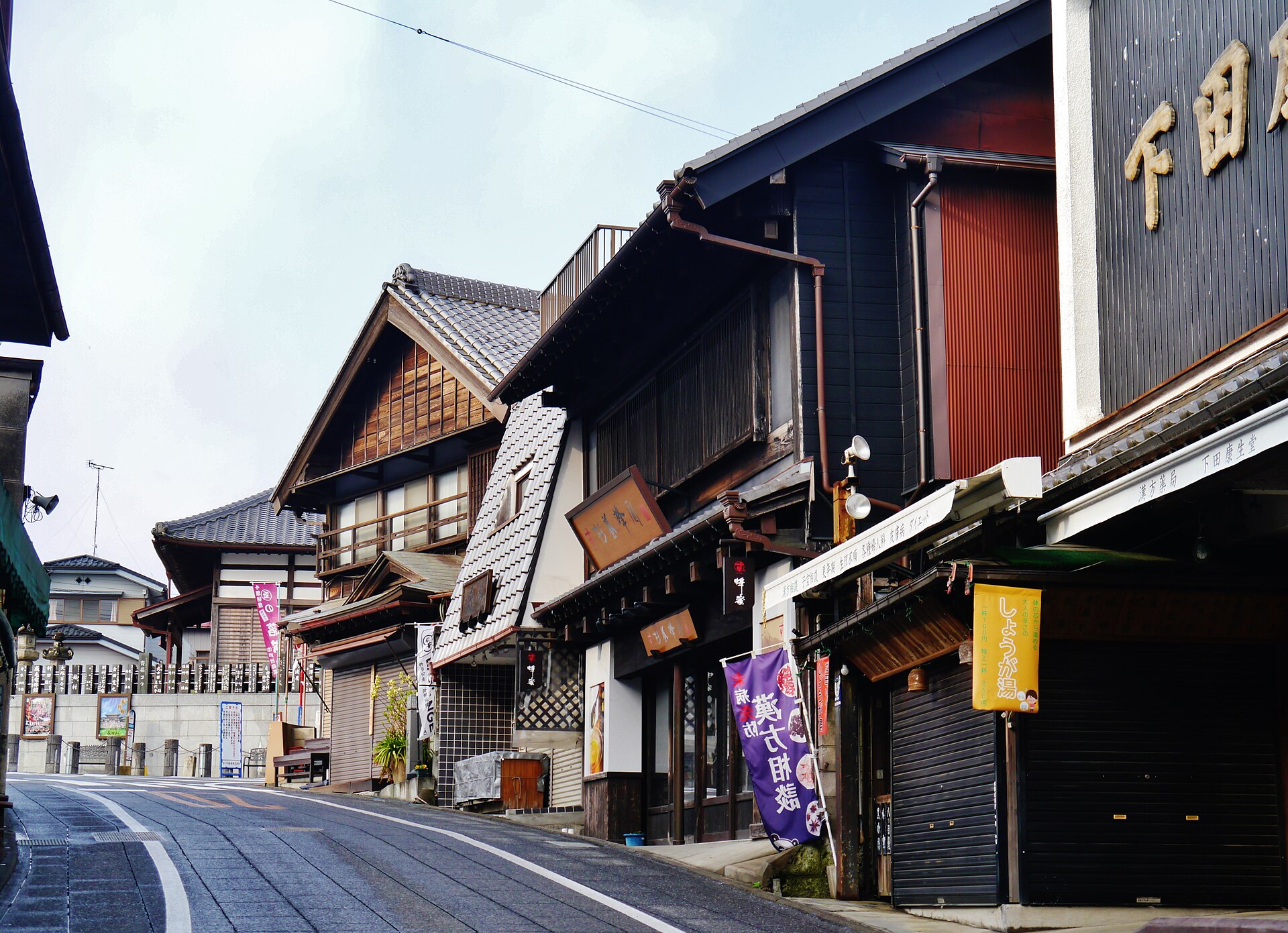 Traditional wooden shopfronts with tiled roofs along the curving Omotesando approach street in Narita
