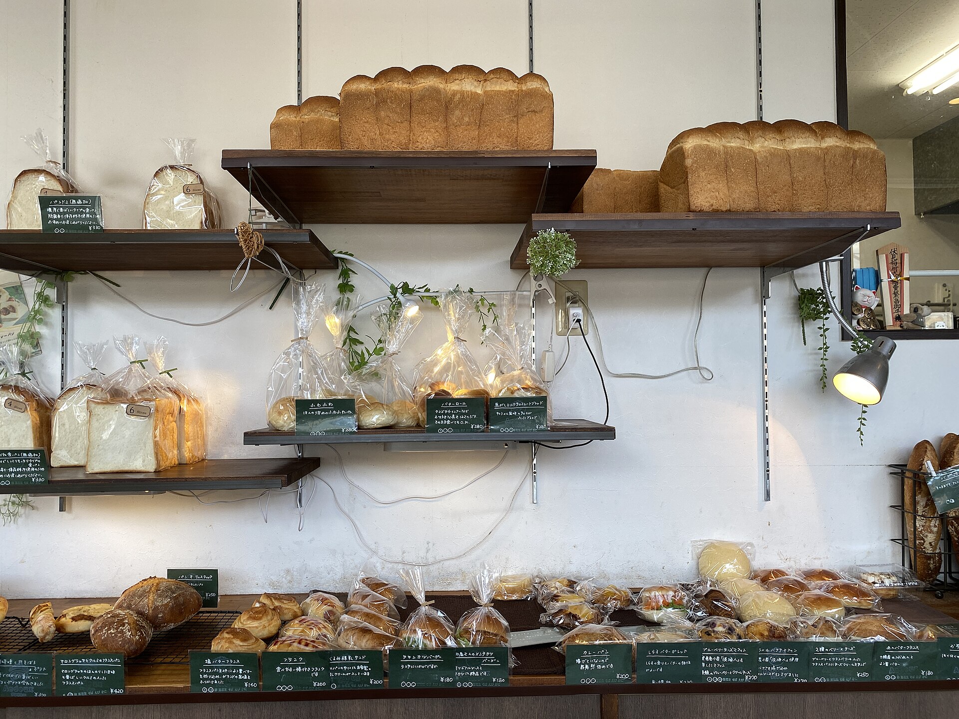 Tall rectangular loaves of Japanese shokupan bread on wooden shelves above a counter of pastries in a bakery