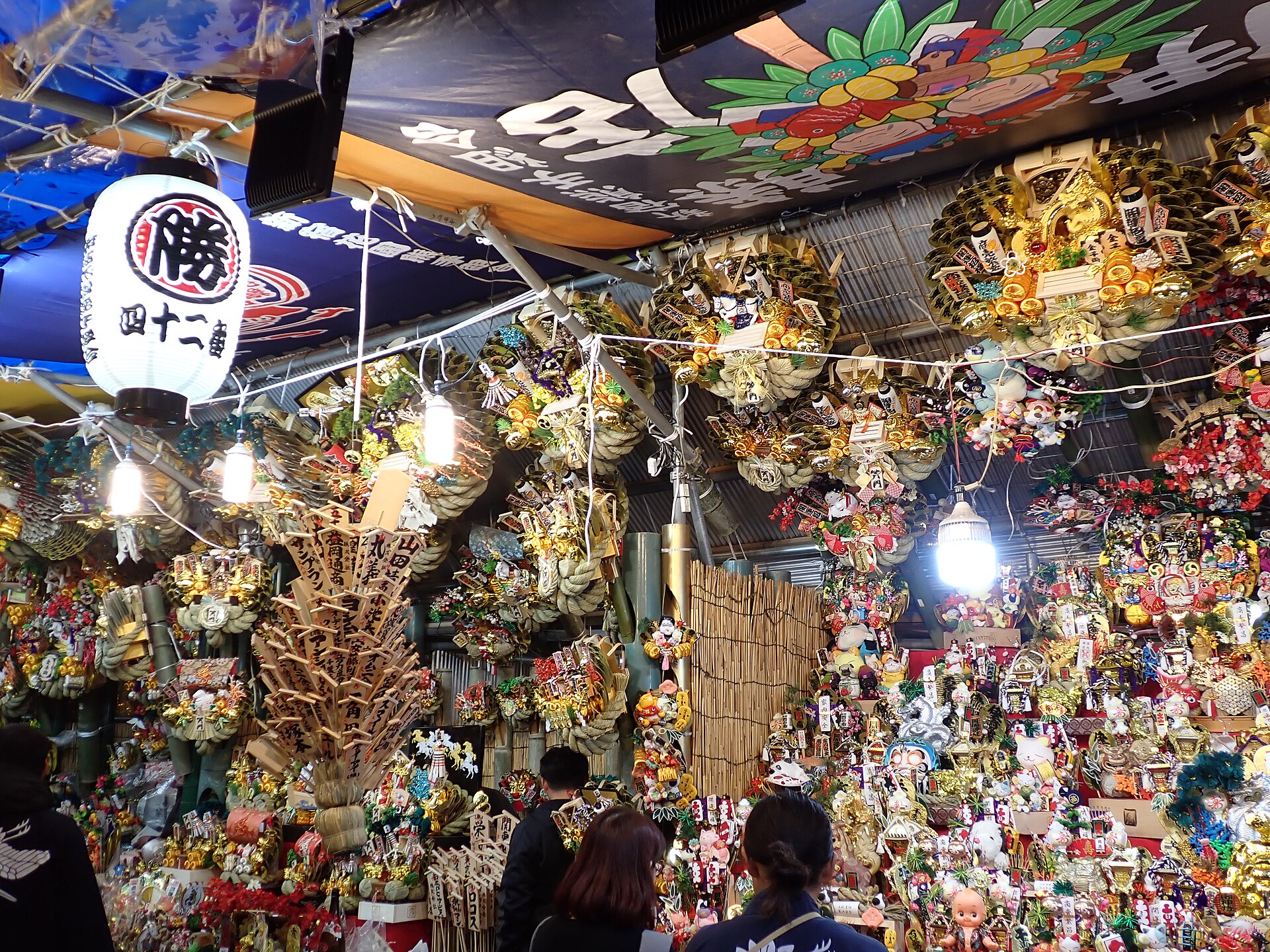 A stall hung with ornate gold and red kumade rakes at a Tori no Ichi shrine market