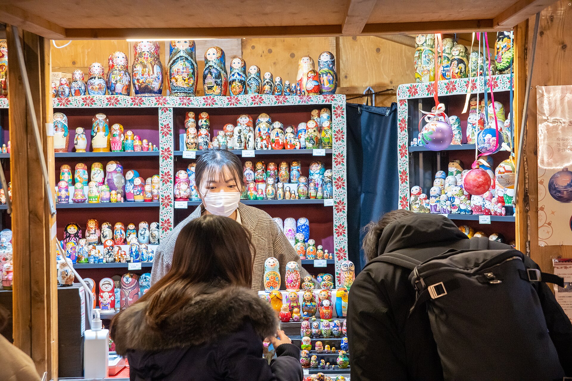 A wooden Christmas market hut stacked with painted matryoshka dolls and glass baubles