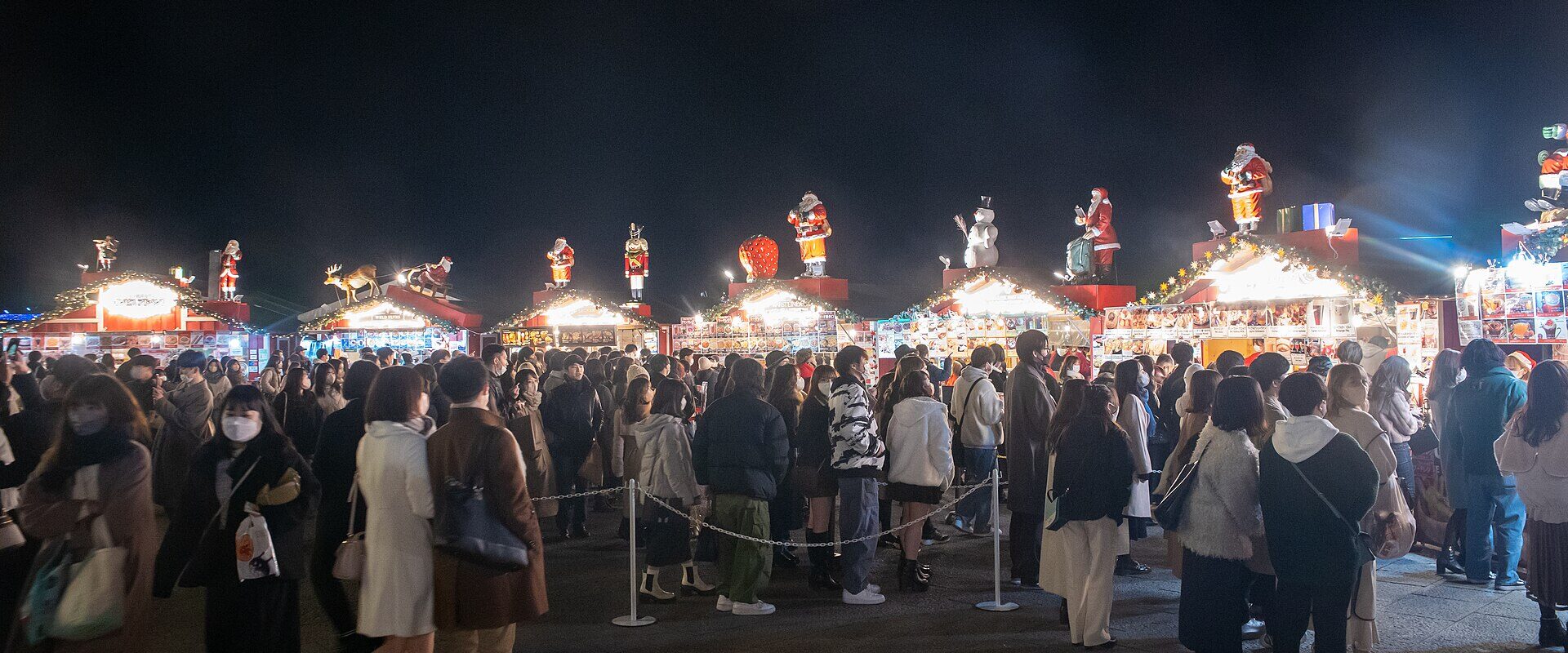 Lit wooden huts topped with Santa figures and a large crowd at the Yokohama Red Brick Warehouse Christmas market