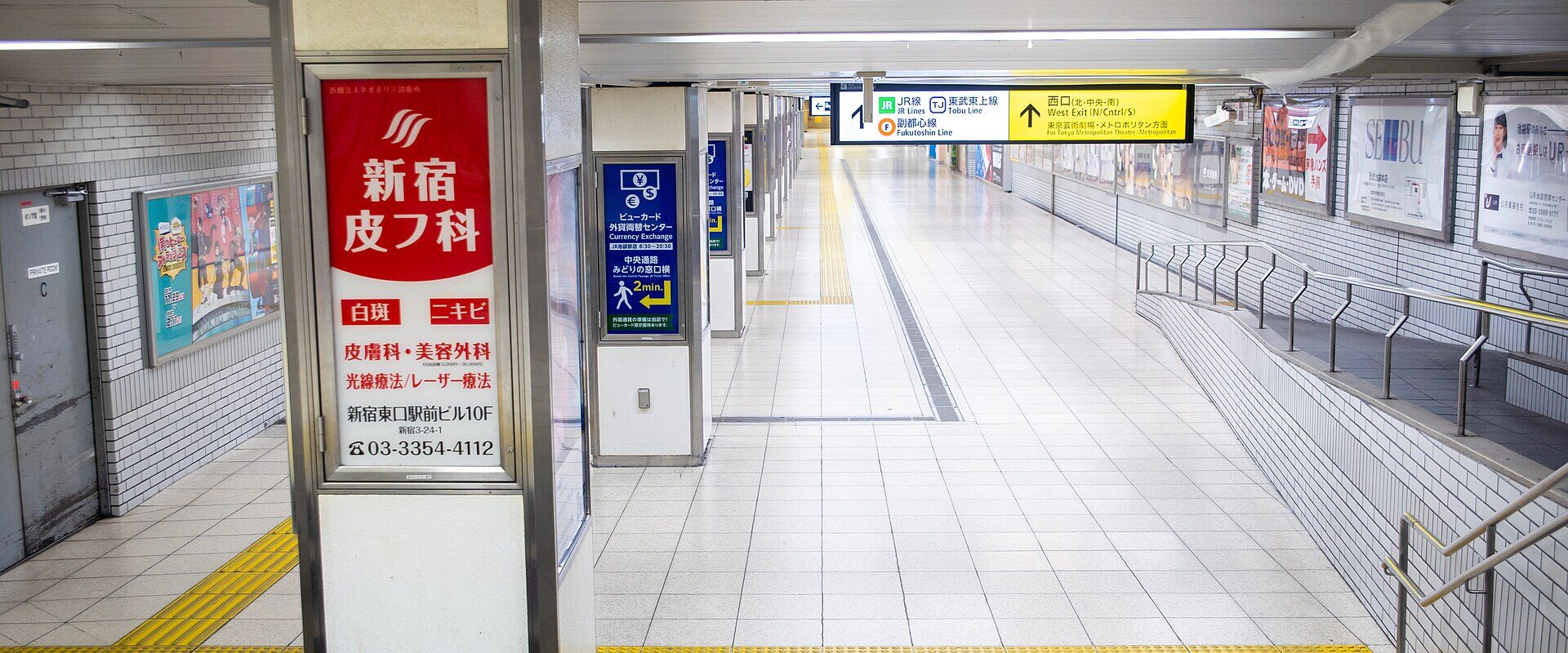 A wide underground passage at Ikebukuro Station with yellow tactile paving, a sloped walkway with handrails and bilingual direction signs