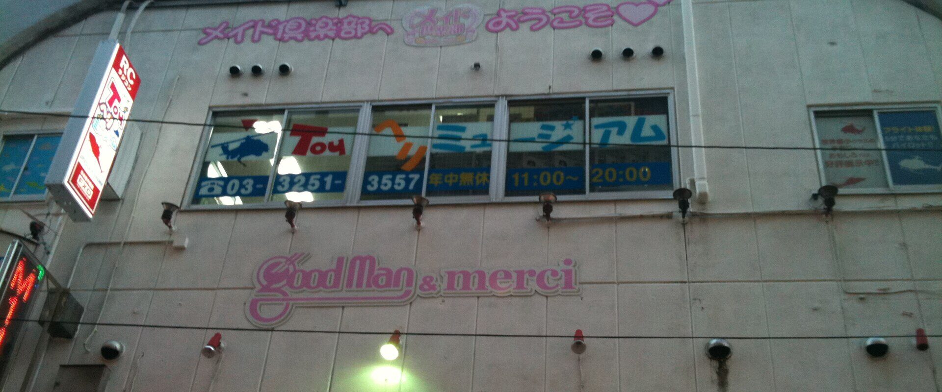 Pink maid club signage on an upper floor of a narrow Akihabara building at dusk