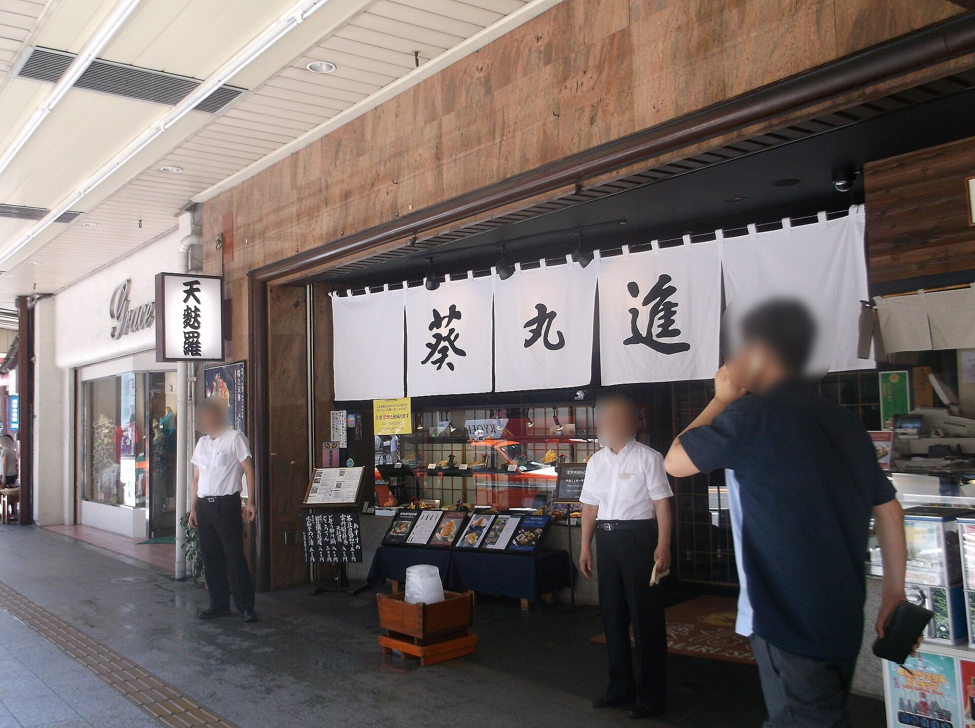 The entrance of a tempura restaurant in Asakusa with white noren curtains, plastic food displays and a lit sign reading tempura