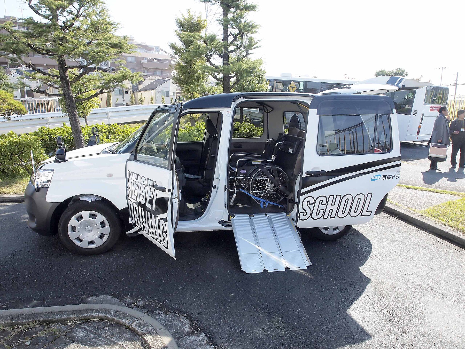 A white JPN Taxi-style vehicle with its side door open and a fold-out ramp leading up to a wheelchair secured inside