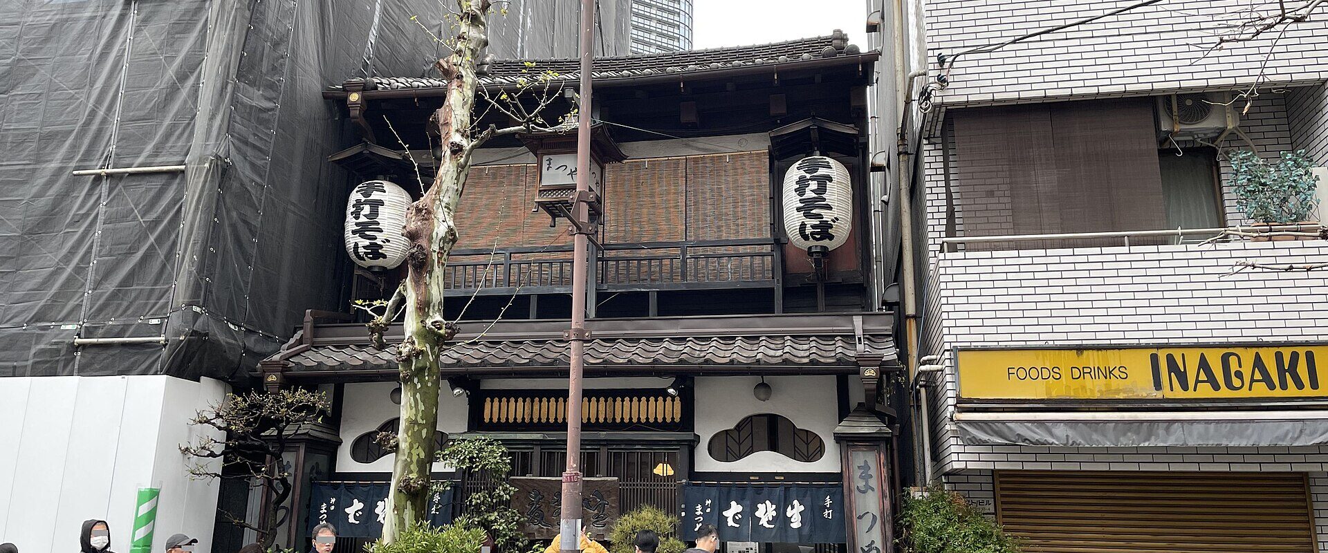 The old two-storey wooden shopfront of Kanda Matsuya soba with white paper lanterns, navy noren curtains and people queuing outside