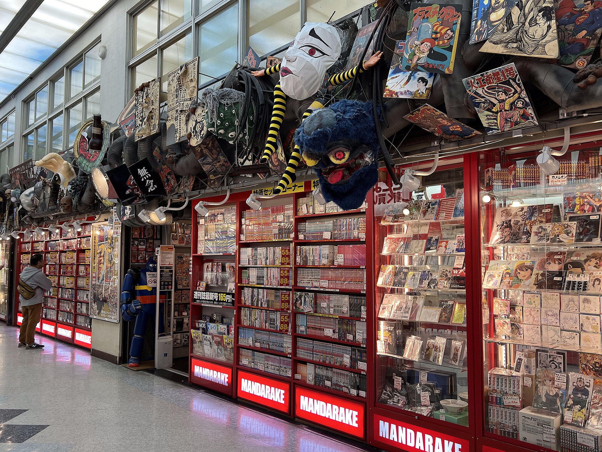 The red-lit shopfronts of Mandarake in Nakano Broadway, with manga shelves and giant papier-mache character heads hanging from the ceiling