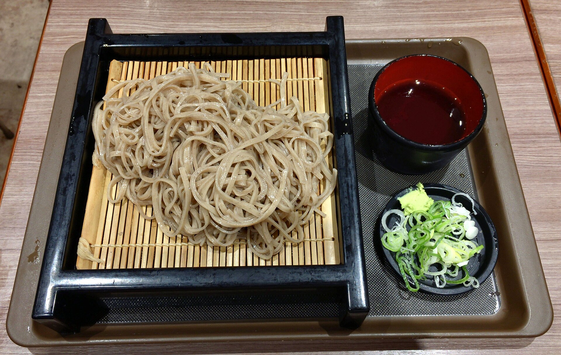 Cold mori soba on a bamboo tray with a cup of dipping sauce, sliced spring onions and wasabi