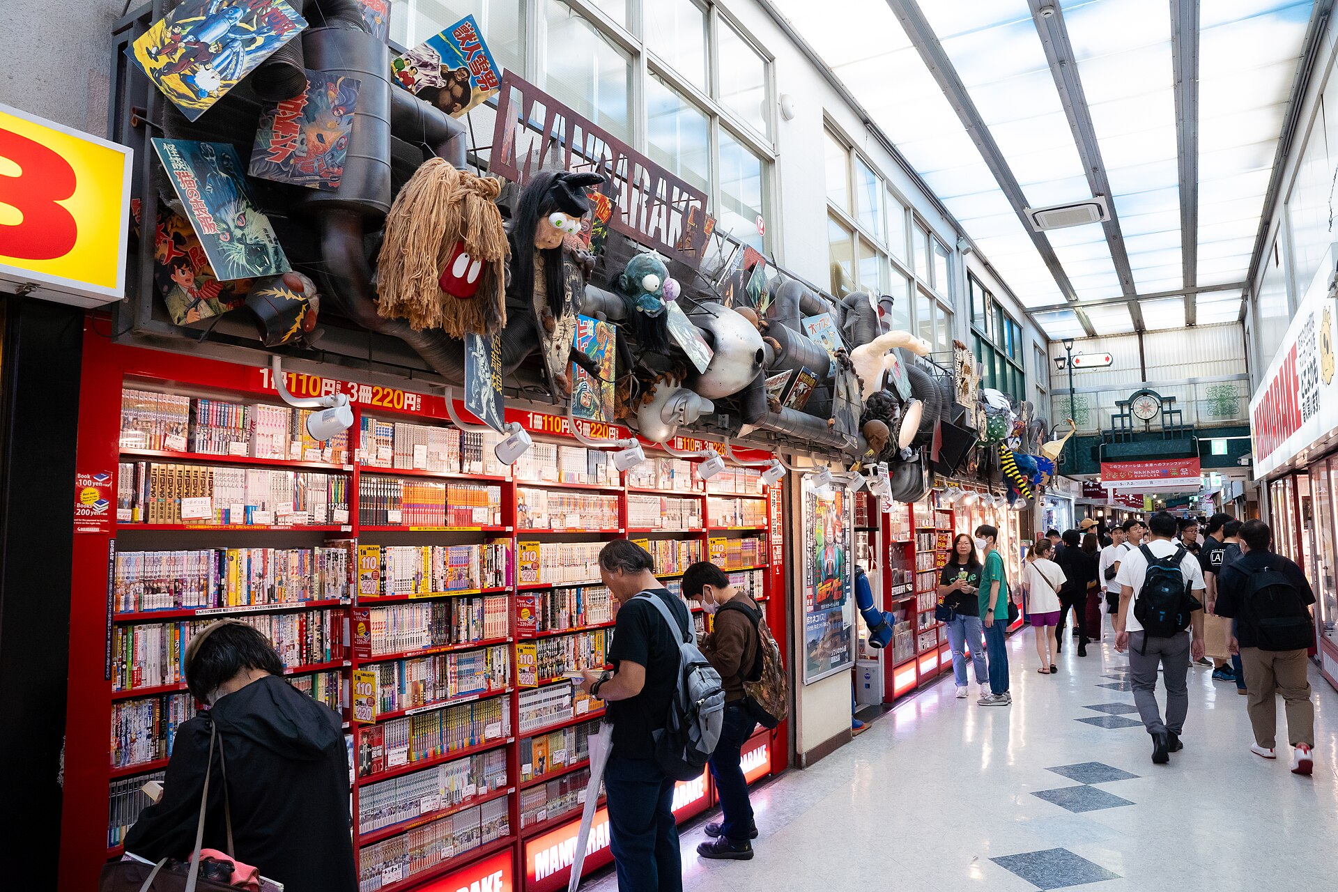 Shoppers browsing red Mandarake manga shelves in a corridor of Nakano Broadway