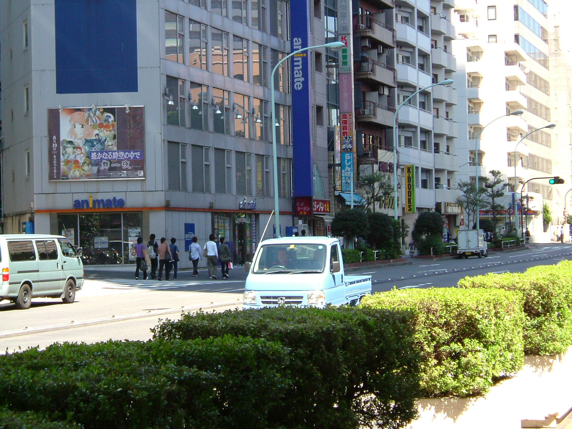 An older Animate store on the corner of a wide Ikebukuro street with a large anime poster on its facade and K-Books signs further along