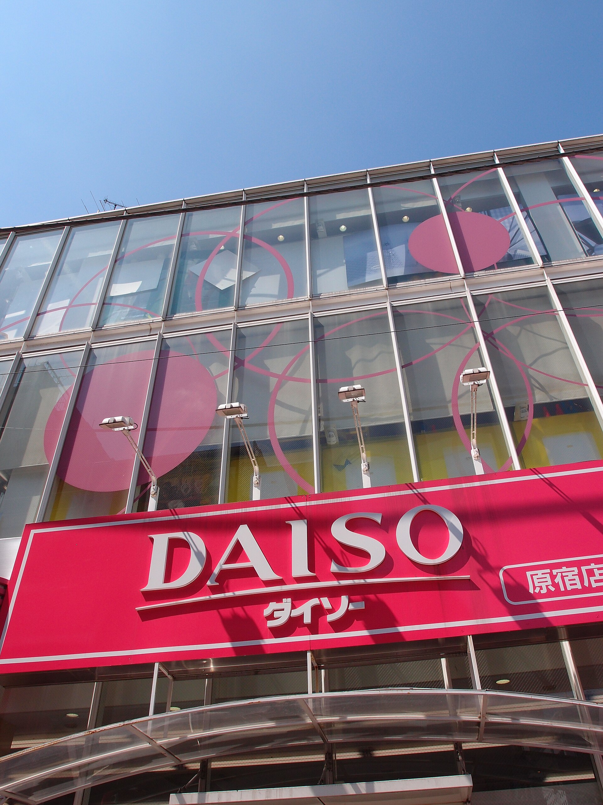A red Daiso sign marks the Harajuku shopfront on Takeshita Street, beneath glass windows decorated with pink circles.