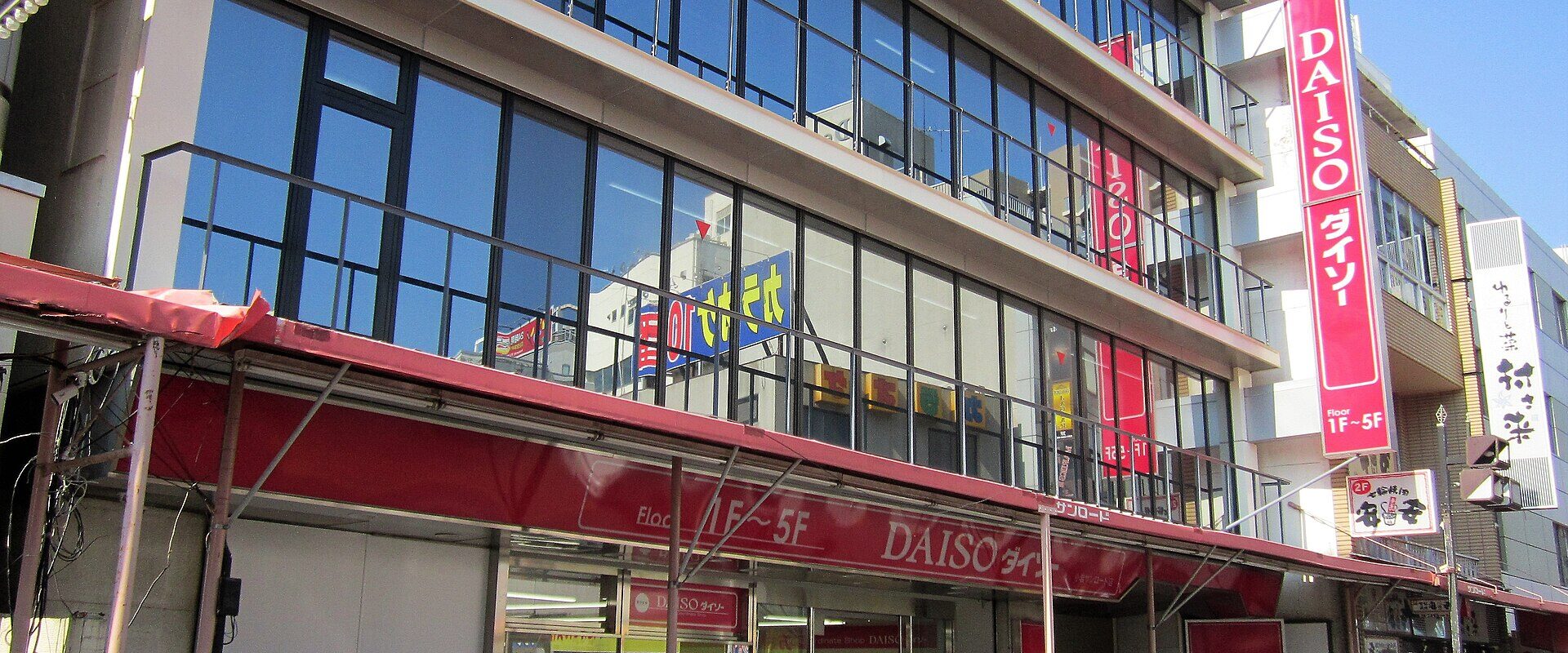 Red Daiso signs mark a glass-fronted shop in Koiwa, Tokyo, with bicycles parked along the entrance.