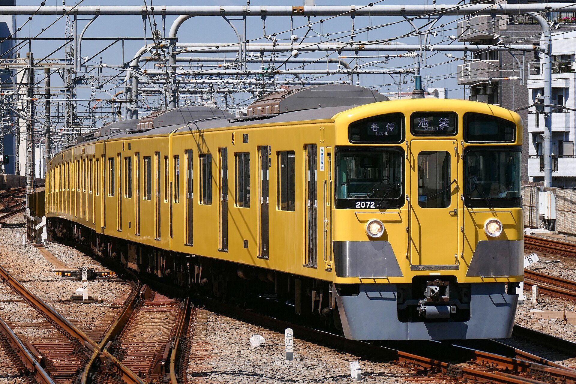 A yellow Seibu Railway local train approaching a station with Ikebukuro on its destination board