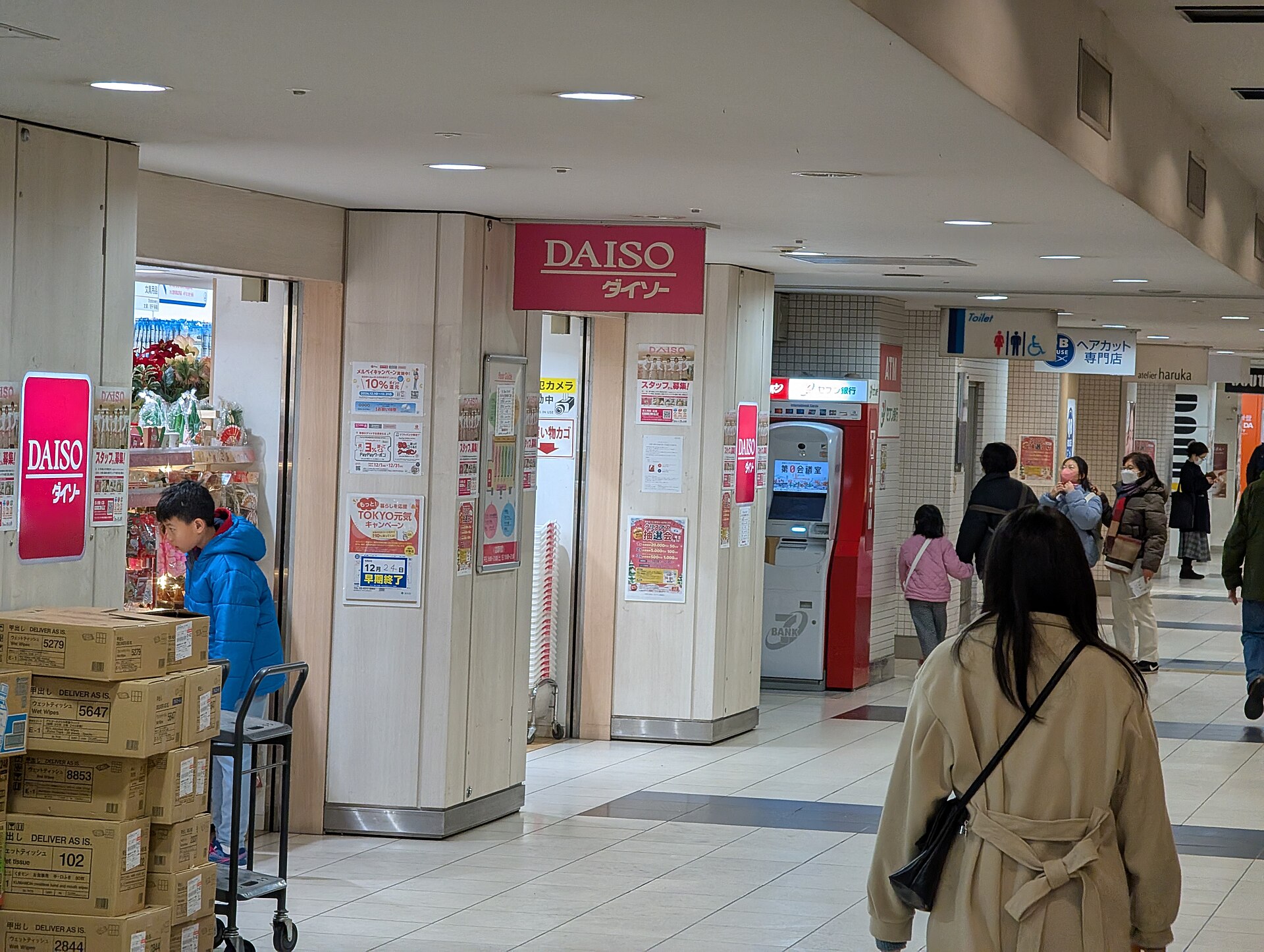 Shoppers pass a red-signed Daiso entrance with merchandise visible inside Keio Mall Annex in Shinjuku, Tokyo.