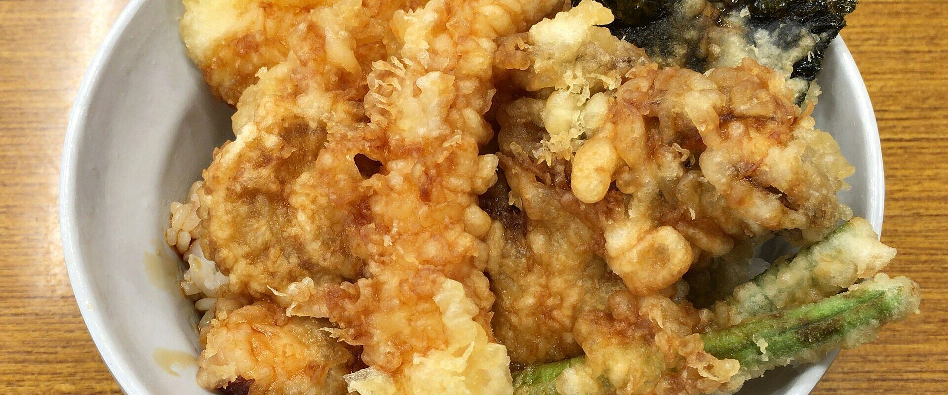 A tendon bowl piled with prawn, fish, vegetable and nori tempura glazed with sweet sauce over rice