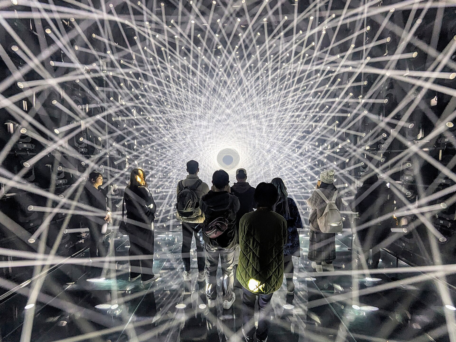 Visitors stand amid dense intersecting white light beams and mirrored reflections at teamLab Borderless in Tokyo's Azabudai Hills.