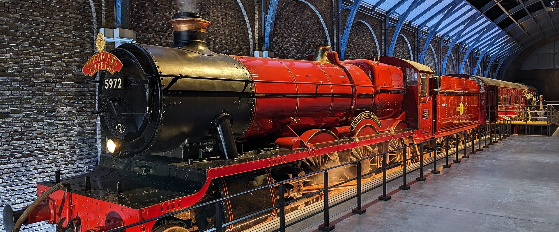 The red and black Hogwarts Express steam locomotive standing at a platform under an iron and glass station roof